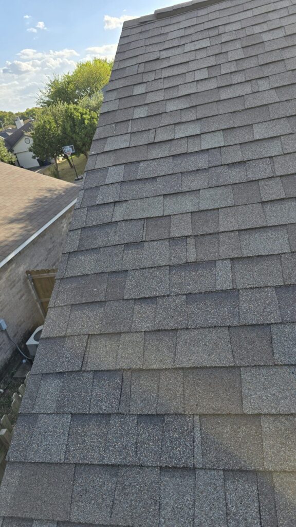 Finished asphalt shingle roof on a steep slope with clean, aligned shingle rows.