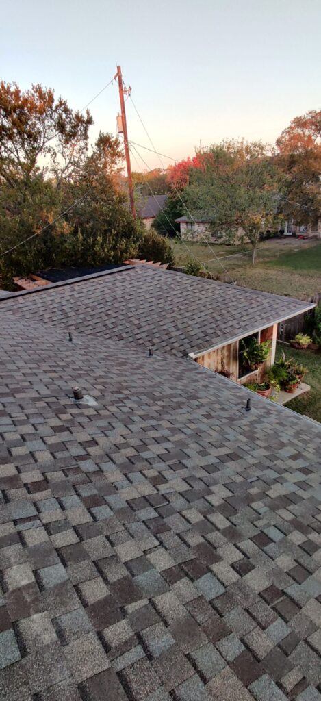 Roof ridge line after new shingle installation with crew working in Caldwell, Texas.
