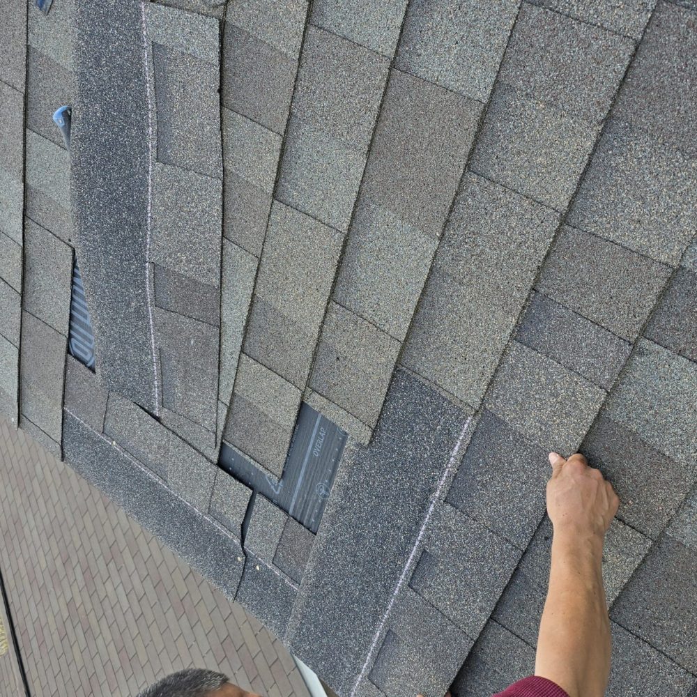 Roofer inspecting asphalt shingles near a roof vent during installation work.