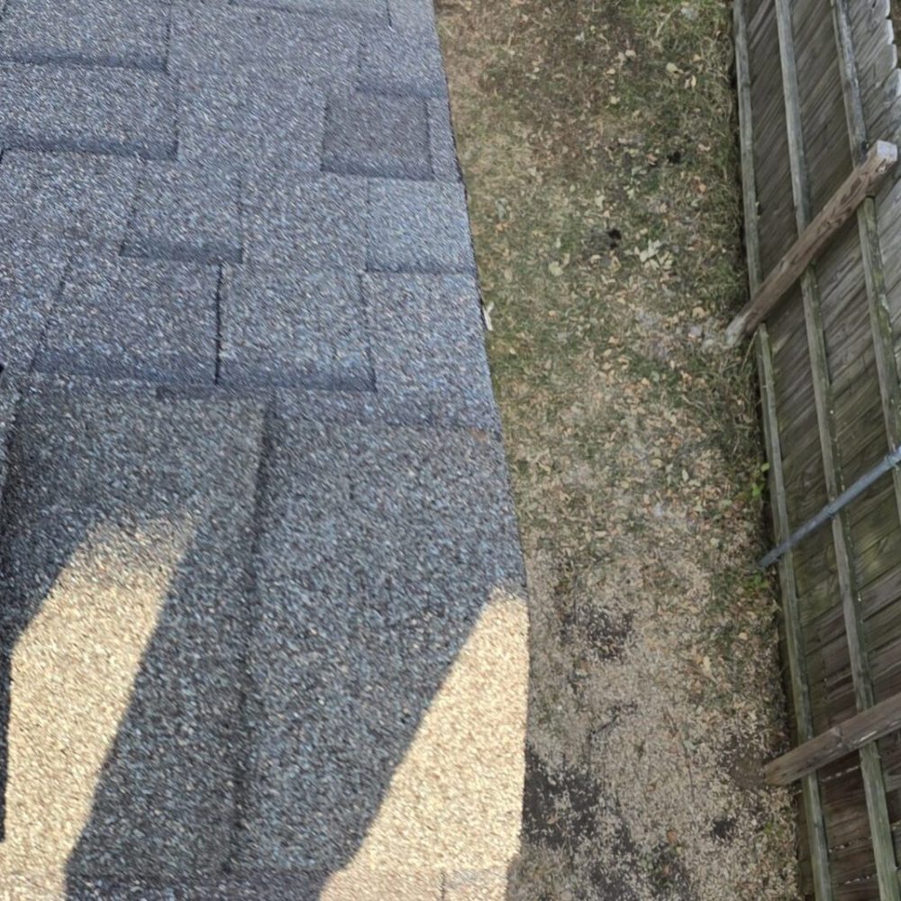 View from rooftop showing newly installed shingles near the roof edge beside a wooden fence.